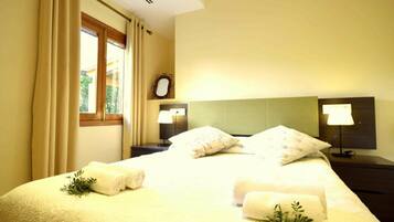 A hotel room with a bed, two bedside lamps, a nightstand, a window with curtains, and a mirror on the wall.