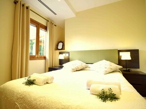 Ein Hotelzimmer mit Bett, zwei Nachttischlampen, einem Nachttisch, einem Fenster mit Vorhängen und einem Spiegel an der Wand.