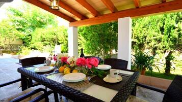 An outdoor patio with a table set for dining, surrounded by wicker chairs and a wooden pergola.
