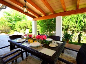 Eine Terrassengruppe im Freien mit Esstisch, umgeben von Korbstühlen und einer Holzpergola.