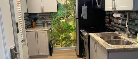 Una cocina moderna con gabinetes blancos, electrodomésticos de acero inoxidable y un salpicadero con un mural de plantas tropicales.