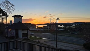 A sunset view from a balcony overlooking a road with a building in the foreground and a body of water in the distance. - Cozy dog friendly studio condo near Lake Hamilton (Hot Springs)
