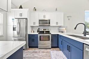 A modern kitchen with white cabinets, stainless steel appliances, and a blue accent wall. - Mariner Lakes 14 Serenity & Sandy Shores (Orange Beach)