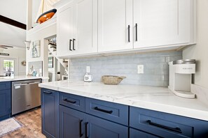 A modern kitchen with white cabinets, a marble countertop, and a built-in dishwasher. - Mariner Lakes 14 Serenity & Sandy Shores (Orange Beach)