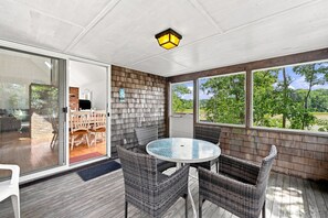 Eine überdachte Terrasse mit Glastür zu einem Essbereich, Korbmöbeln und Blick ins Grüne.
