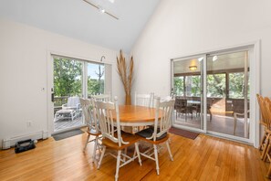 A dining area with a wooden table and chairs, large windows, and a view of the outdoors. - Hidden Haven - Private Mill Pond Getaway (Chatham)