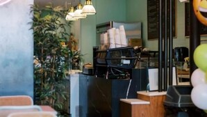Interior de un restaurante con mostrador, zona de mesas y lámparas colgantes.