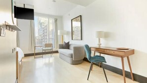 Una habitación de hotel moderna con una televisión de pantalla plana, un sofá, un escritorio con una silla y una ventana con vistas a edificios.