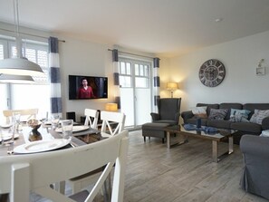 A living room with a television, a sofa, a coffee table, and a dining area with chairs and a table set for two. - Bonde Hus Henny (Büsum)