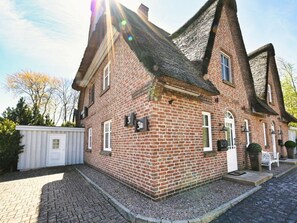 A brick house with a steeply pitched roof, a white door, and a small porch area. - Bonde Hus Henny (Büsum)