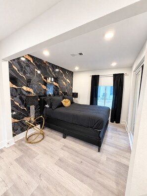 Een moderne slaapkamer met een marmeren wand, een zwart bed en een houten vloer.