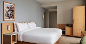 Ein Hotelzimmer mit einem großen Bett, einem Nachttisch, einem Kleiderschrank und einem gerahmten Bild an der Wand.