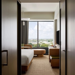 A hotel room with a large window, a bed, a sofa, a desk, and a TV. - King Room | The Atlas Hotel | 0.4 Miles to Harvard Stadium (Boston)