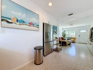 Eine moderne Küche mit einem Edelstahl-Kühlschrank, einer Mülltonne und einem Essbereich mit einem gelben Sofa und einem kleinen Tisch.