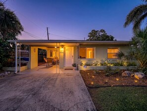A single-story house with a covered porch, a visible door, and a small garden area with plants and rocks. - Barefoot Bungalow - Stroll to beach (Treasure Island)