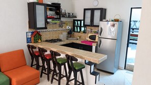 A kitchen with a bar stool area, a refrigerator, and a microwave.