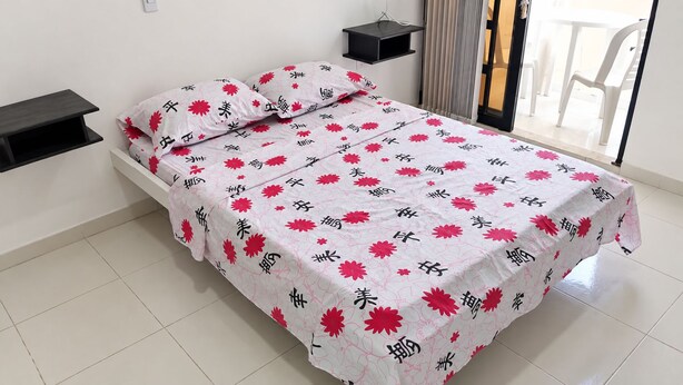 Een bed met een bloemenprint, een nachtkastje en een stoel, zichtbaar door een raam.