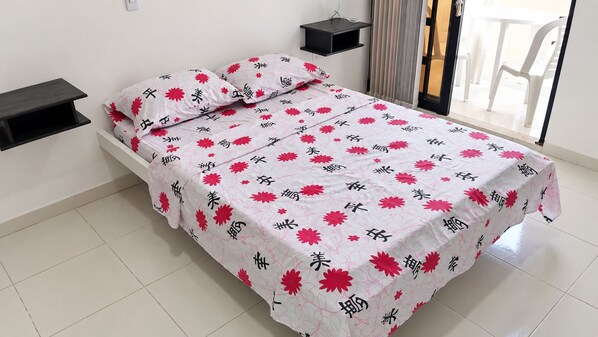 Ein Bett mit Blumenmuster, ein Nachttisch und ein Stuhl sind durch ein Fenster sichtbar.