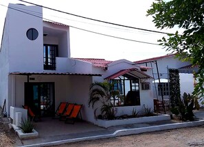 A two-story building with a flat roof, a covered porch, and a small garden area with plants and a bench.