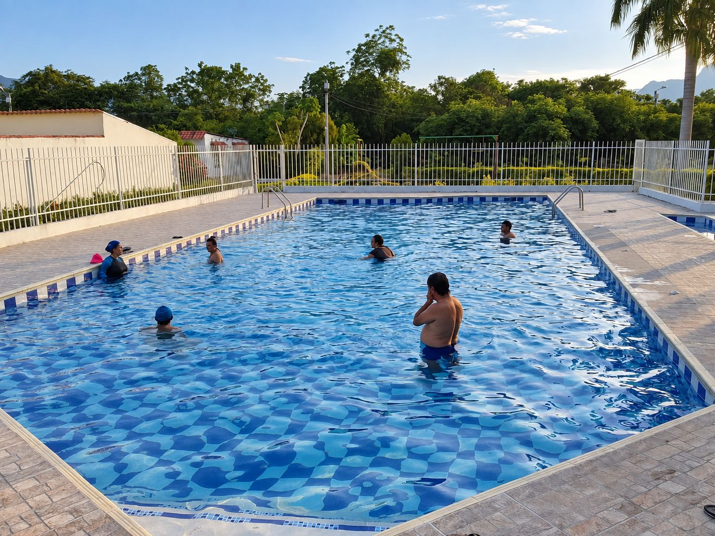 A swimming pool with a tiled deck and a metal fence.