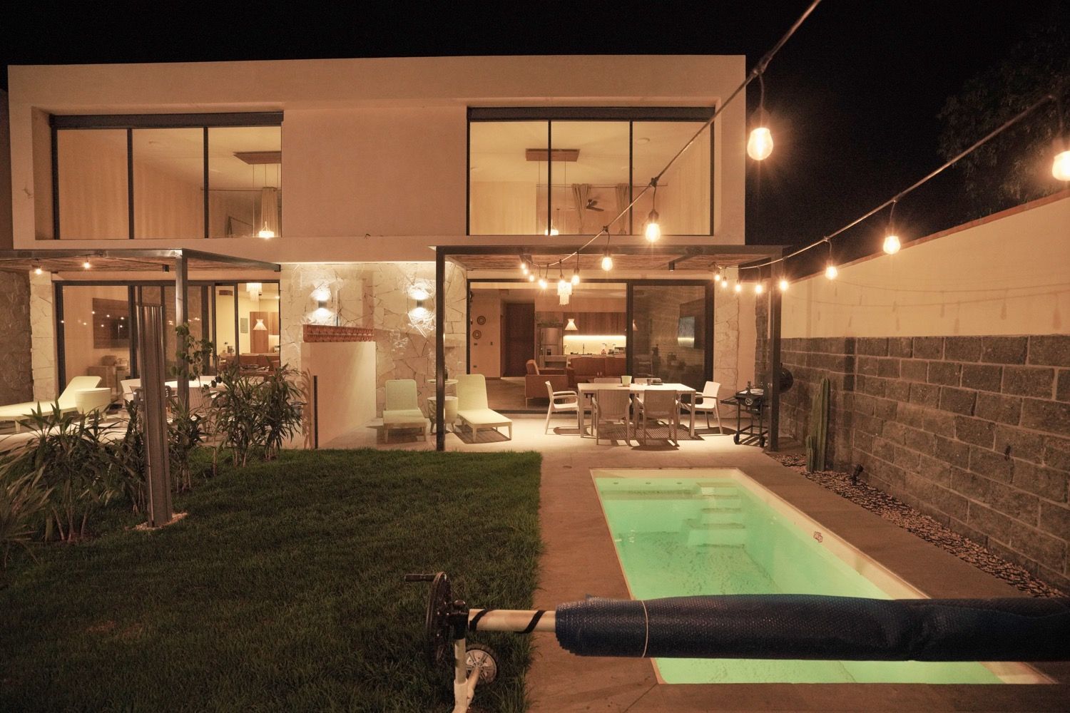 Uma casa moderna com piscina, área de estar ao ar livre e um pátio bem iluminado.