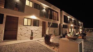 Un edificio moderno con múltiples ventanales y puertas, iluminación exterior y plantas en macetas.