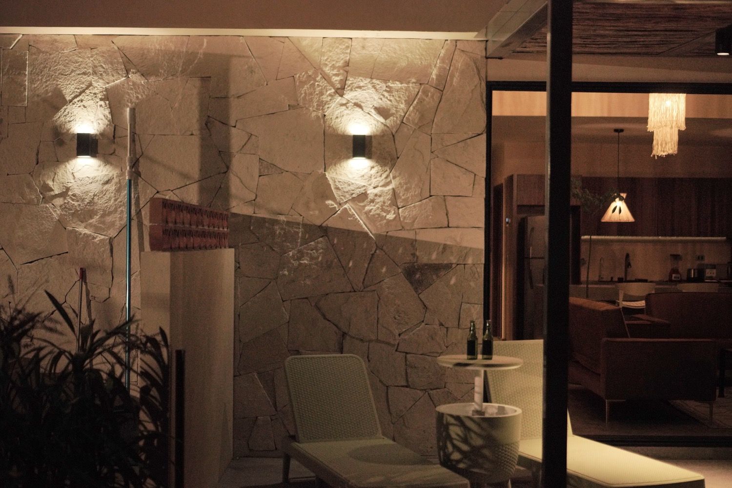 Un interior moderno con una pared de piedra, una zona de estar con una silla y una mesita, y una lámpara colgante.