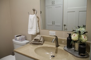 A bathroom with a beige sink, a mirror, a towel rack, a toilet, and a vase with flowers. - Enjoyable 5-bedroom house with AC in welcoming Wellman (Wellman)
