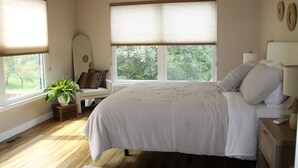 Ein Schlafzimmer mit einem Bett, Nachttischen, einer Zimmerpflanze und einem Fenster mit Jalousien.