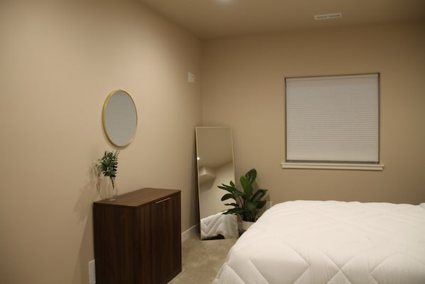 A bedroom with a bed, a dresser, a mirror, and a window with blinds.