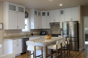 A modern kitchen with white cabinets, stainless steel appliances, and a central island with bar stools. - *Nature* clean* spacious* five bedroom* 3 bathroom . (Wellman)