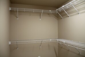 A corner of a room with a beige wall and a white metal rack with multiple hooks.