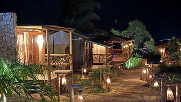 Caminho que leva a um edifício rústico com fachada de pedra, deck de madeira e iluminação ambiente.