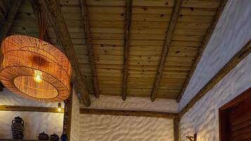 Una cama con colcha blanca, una lámpara de fibra trenzada arriba y techo de madera rústica.