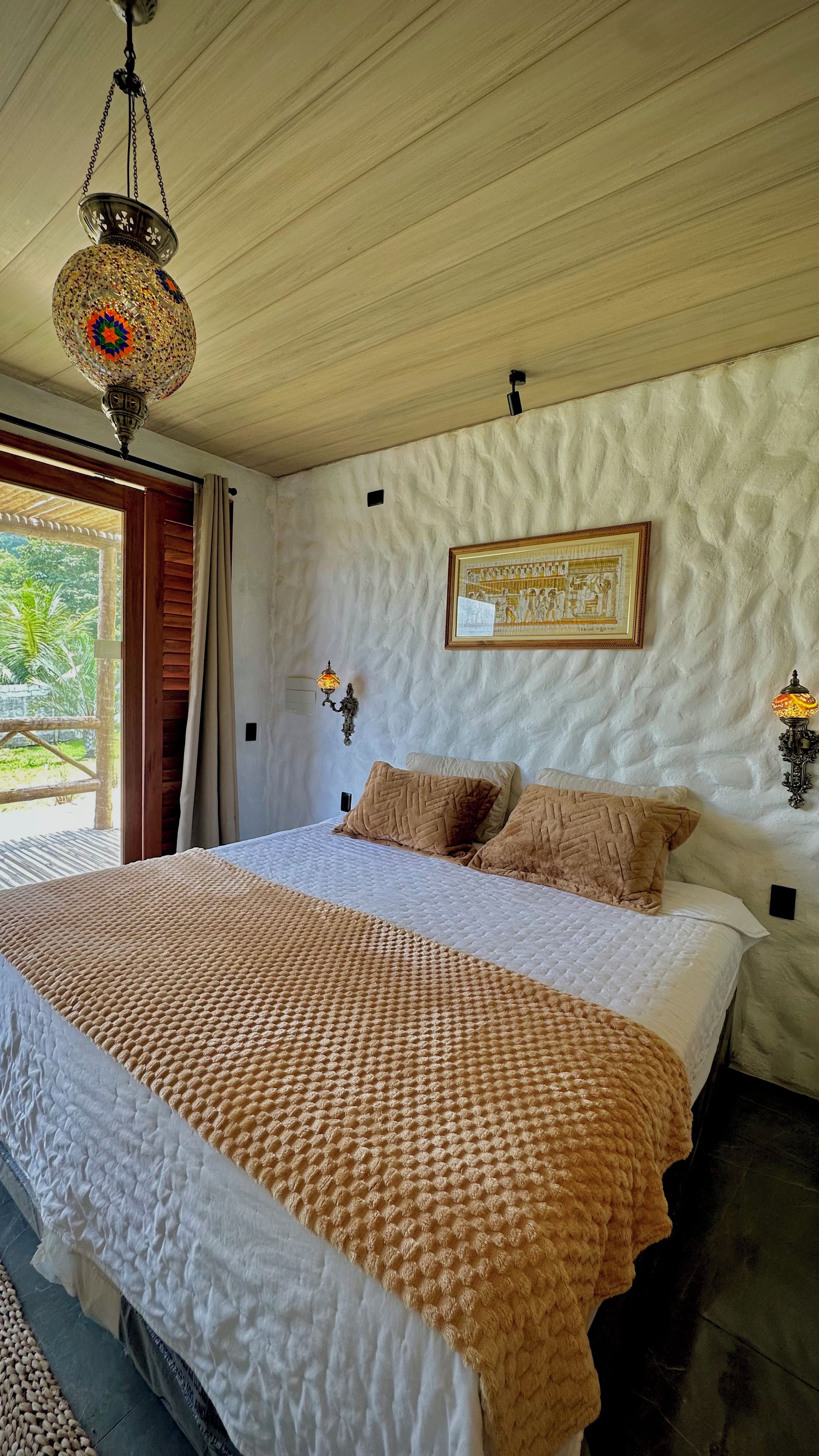 Un dormitorio con una cama grande, una lámpara colgante y un cuadro en la pared.