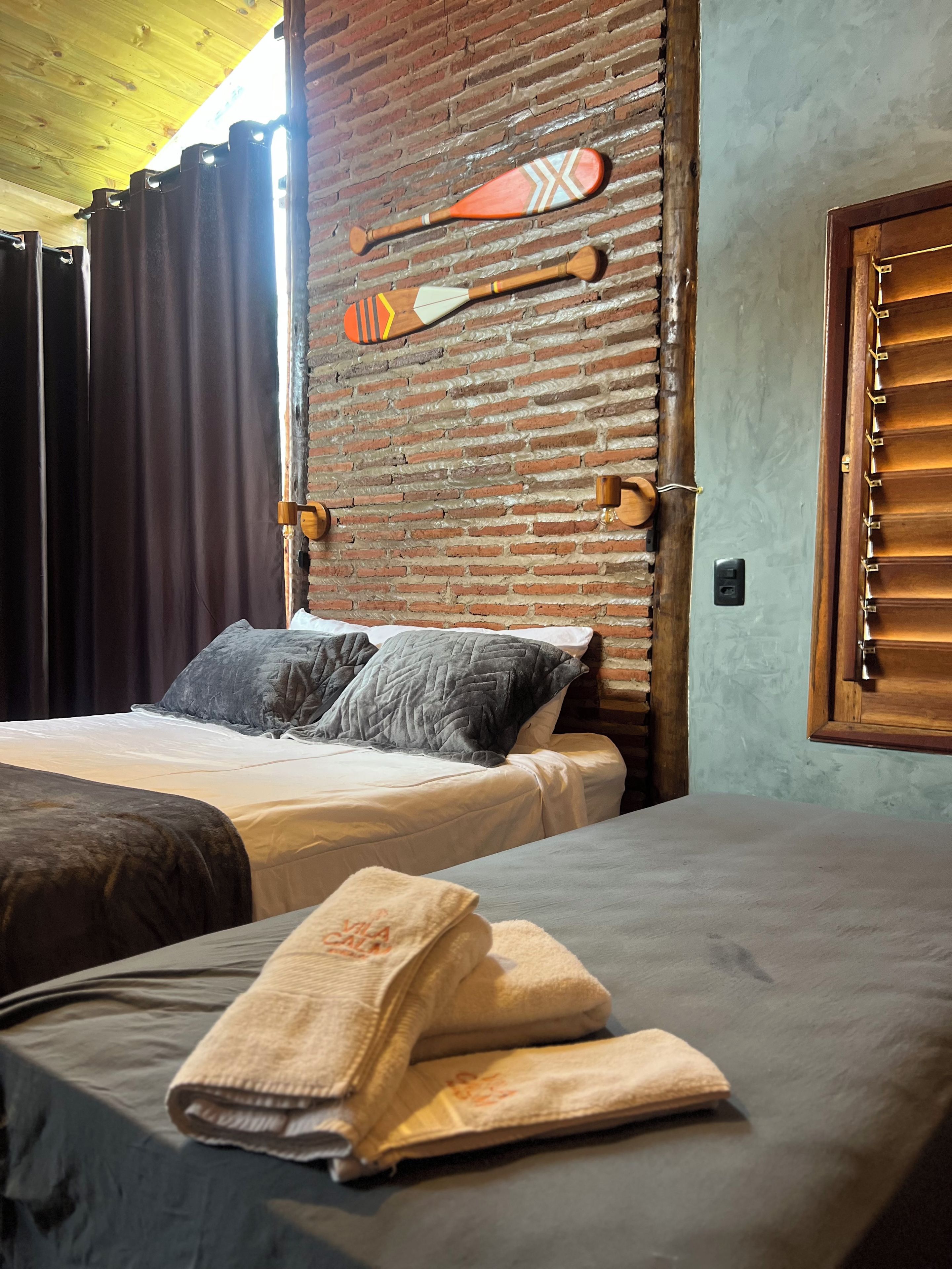 A hotel room with a bed, pillows, a wooden wall with a paddle, and a window with blinds.