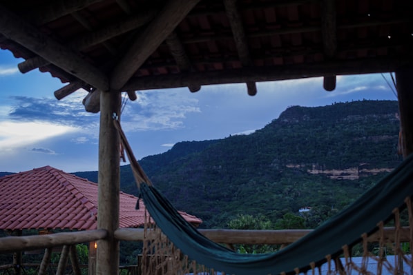 A hammock under a wooden structure with a view of a mountainous landscape.