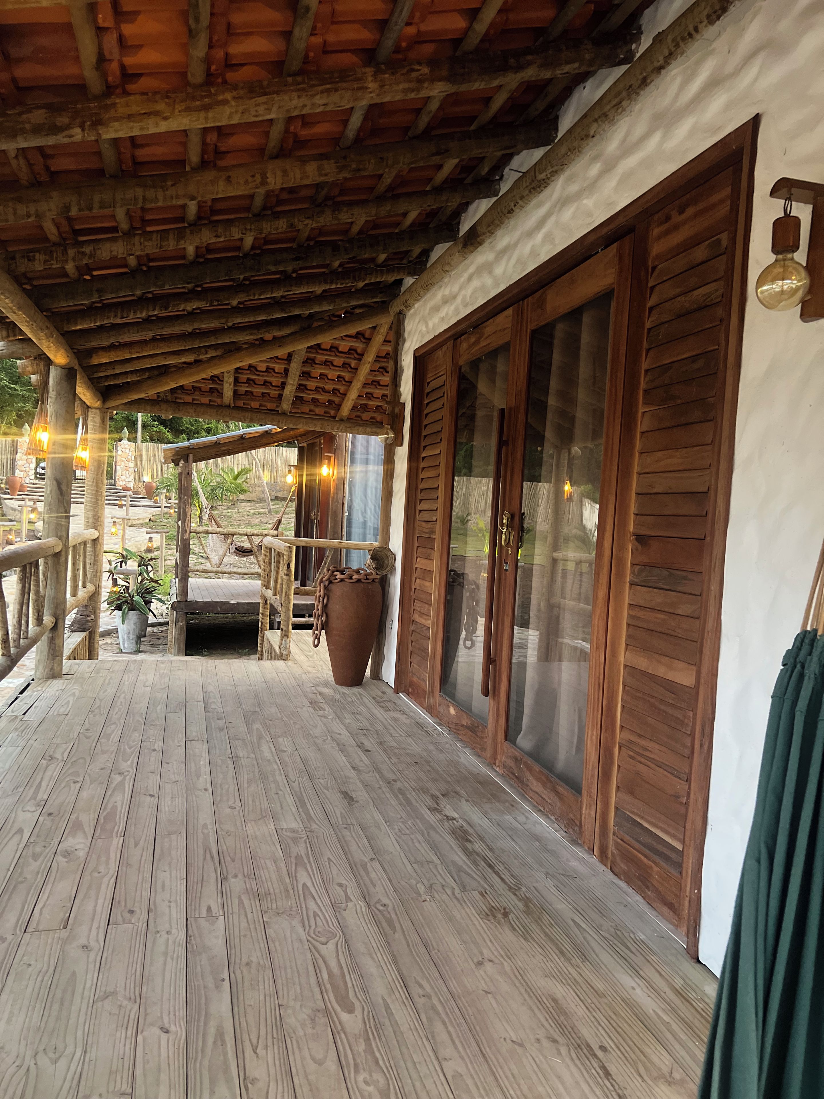 Una terraza de madera con techo rústico, una planta grande en maceta y vistas al exterior.