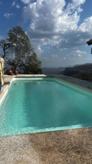 A rectangular pool with clear water, surrounded by a stone deck, and a view of distant hills under a partly cloudy sky.