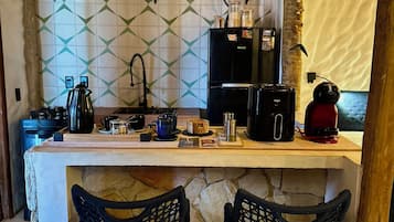 Una cocina con encimera de piedra, dos taburetes de mimbre, una cafetera y un refrigerador.