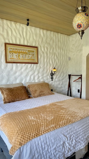 A bed with a quilted cover, a wall-mounted lamp, and a framed picture.