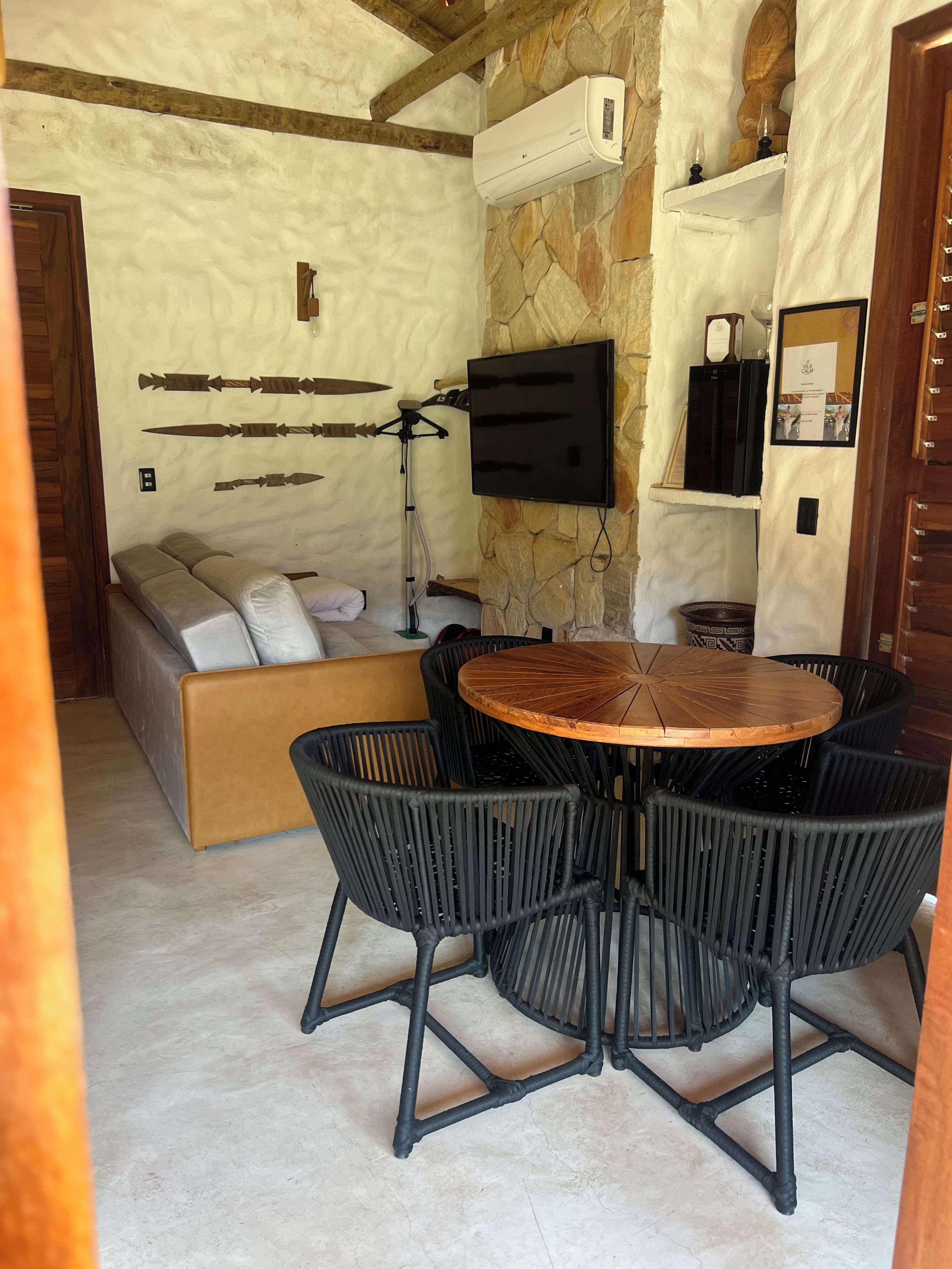 A cozy living area with a stone wall, a mounted TV, a sofa, and a round wooden table with chairs.