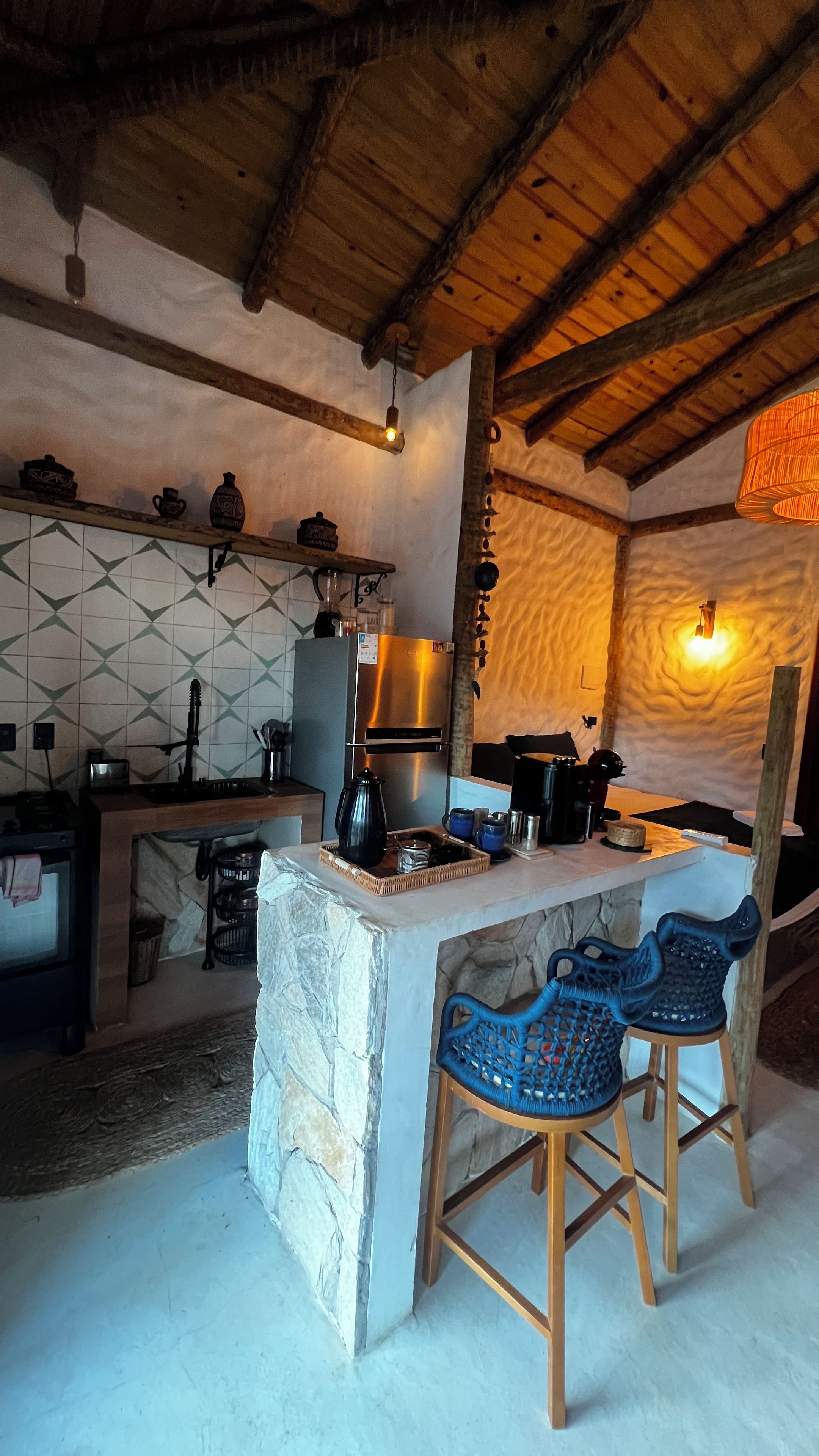 A rustic kitchen with a stone island, wooden bar stools, and a hanging light fixture.
