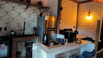 A rustic kitchen with a stone island, wooden bar stools, and a hanging light fixture.