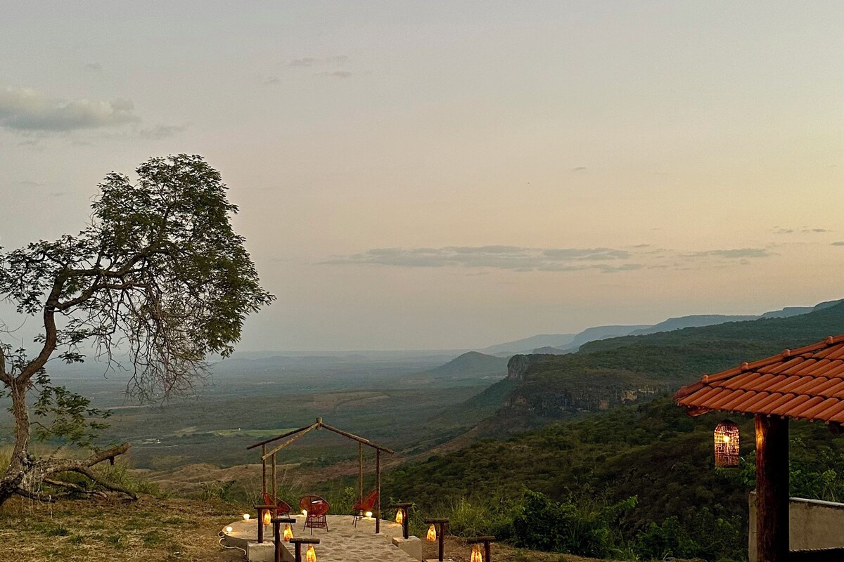 A pool with a clear view of the surrounding landscape, a stone structure with a tiled roof, and a tree.