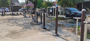 An outdoor gym area with exercise equipment, a covered seating area, and a parking lot with cars. - Cozy 1-bedroom condo with Hot, Cold, Water and AC in lovely
Chiang Mai Thailand (Tambon San Na Meng)