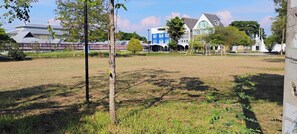 A grassy field with trees and a building in the background. - Cozy 1-bedroom condo with Hot, Cold, Water and AC in lovely
Chiang Mai Thailand (Tambon San Na Meng)