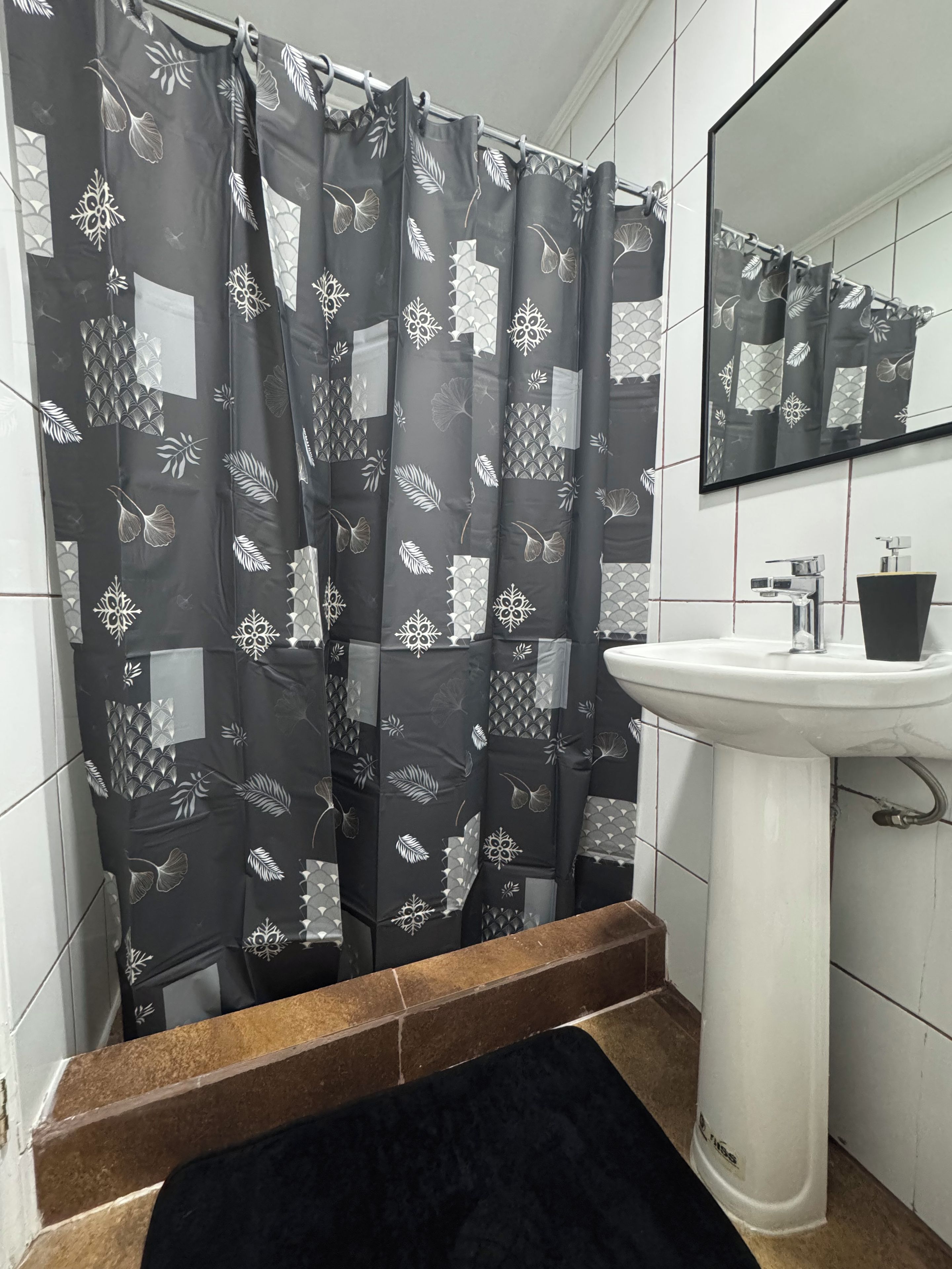 A bathroom with a shower curtain featuring a leaf pattern, a white sink, and a mirror above it.