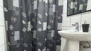 Une salle de bain avec un rideau de douche orné d’un motif de feuilles, un lavabo blanc et un miroir au-dessus.