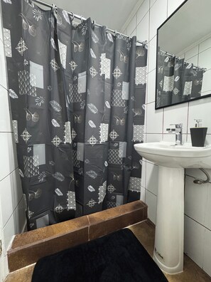 A bathroom with a shower curtain featuring a leaf pattern, a white sink, and a mirror above it. - Tranquil studio with AC in beautiful Talca city center (Talca)